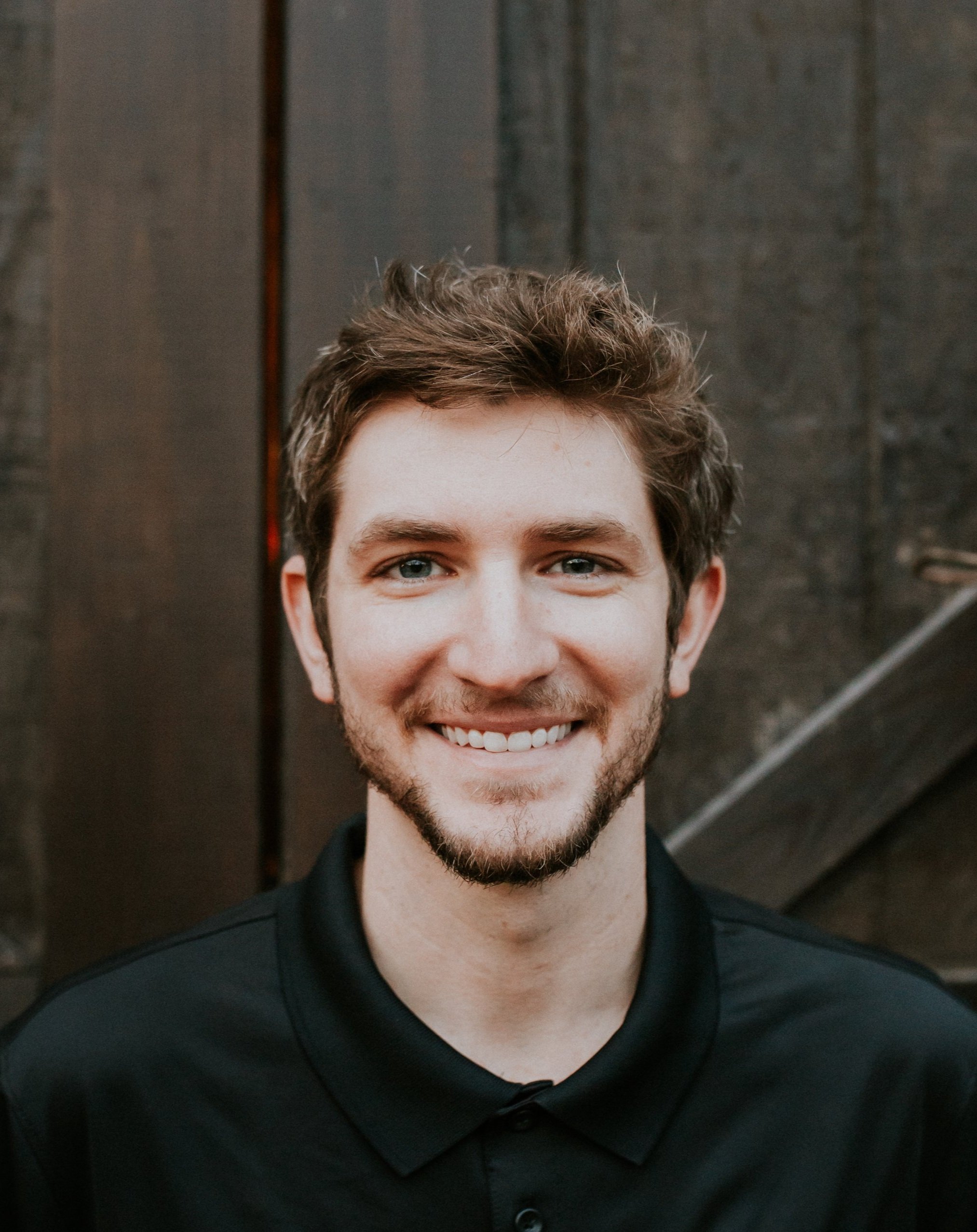 Portrait of Taylor MacMillan, smiling, with brown wavy hair and a beard.